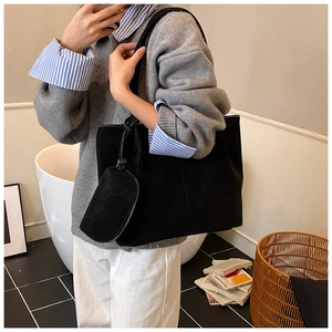 Detail of a black suede tote bag featuring white contrast stitching and mini pouch