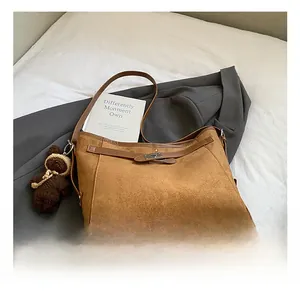 Close-up of brown matte leather shoulder bag with metal buckle and teddy bear charm