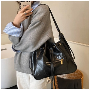 Detail of black quilted bucket bag featuring drawstring closure and gold zipper pocket