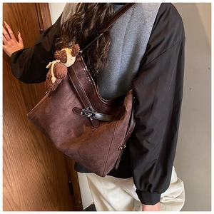 Detail view of brown suede tote bag featuring silver turn-lock and knit bear charm