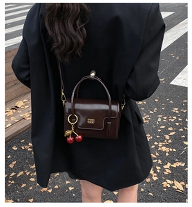 Outdoor shot of a vintage brown leather crossbody bag with a cherry charm and gold hardware