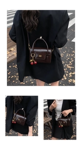 Detail of glossy brown leather crossbody bag with cherry charm and metal logo