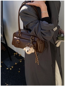 Close-up of dark brown Boston bag with golden hardware and cute plush bear charm
