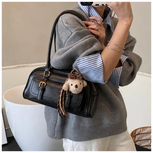 Close-up of black leather bowling bag with metal buckle pocket and plush dog charm