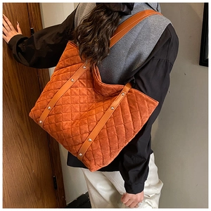 Close-up of orange quilted suede tote bag with brown leather strap and silver rivets
