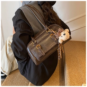 Detail of vintage brown leather bowling bag with gold buckles and teddy bear charm