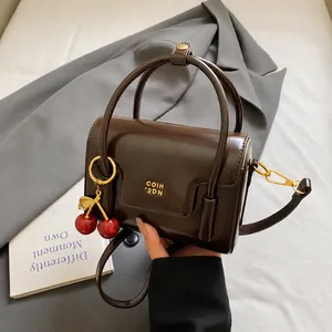 Detail of vintage dark brown handbag with gold logo and cherry charm on grey fabric