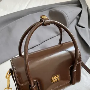 Detail of dark brown glossy leather handbag with gold hardware and round handles