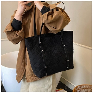 Detail of the quilted texture and silver rivet decorations on the black tote bag