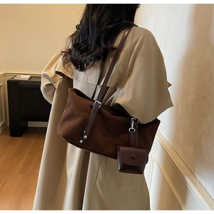 Close-up of brown suede tote bag with leather strap and mini charm purse on a shoulder
