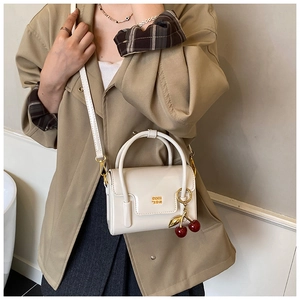 Mini cream patent leather bag with gold logo and cherry charm on a trench coat model