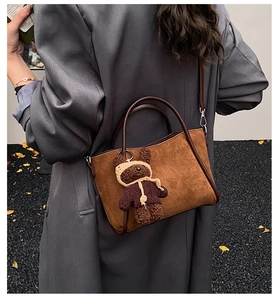 Braune Wildleder-Eimertasche mit Bärenanhänger in einer herbstlichen Straßenszene