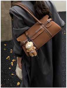 Détail d'un sac Boston en cuir marron avec surpiqûres blanches et pendentif ours décoratif