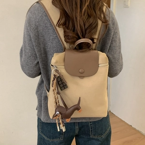 Detail view of khaki nylon backpack featuring brown leather flap and cute dog charms
