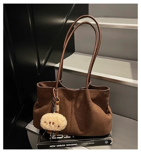 Detail of brown suede tote bag featuring a cute plush sheep pendant on a staircase