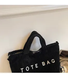 Detail of black corduroy tote bag showing thick ribbed texture and white TOTE BAG embroidery