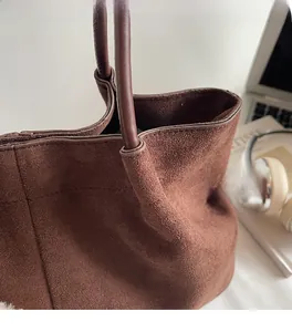 Close-up of brown suede tote bag handles with laptop and lifestyle props