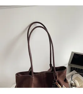 Detail of deep brown suede tote bag with woven knot charm and stylish shoulder straps