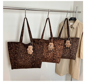Detailed view of leopard print tote bag with plush bear charm hanging on a coat rack