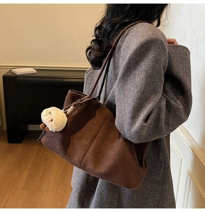 Detail of dark brown suede tote bag with plush charm on gray tweed coat