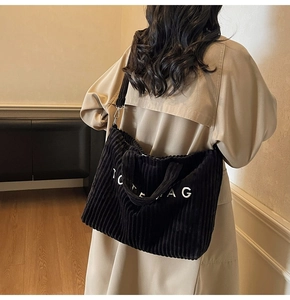 Detail of black corduroy tote bag showing ribbed texture and adjustable strap on a model