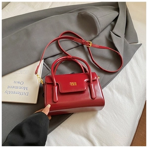 Detail of dark red glossy leather handbag with gold metal logo and adjustable strap