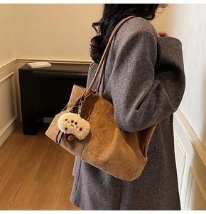 Brown suede tote bag with plush pendant accessory styled on model in grey coat