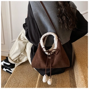 Detail of coffee suede bucket bag with white fleece handle and fluffy pompom charm