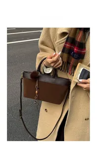 Detail of brown suede tote bag with leather trim and decorative fur ball charm