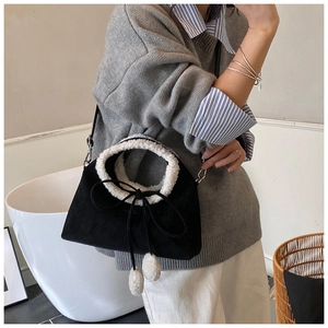 Détail du sac bandoulière en daim noir mat avec poignées en similicuir blanc et pompons