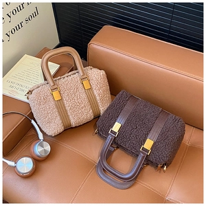 Close-up of plush faux fur Boston bags in beige and coffee with leather handles on sofa