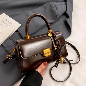 Detalle de bolso de cuero marrón oscuro con cierre dorado y cordón trenzado