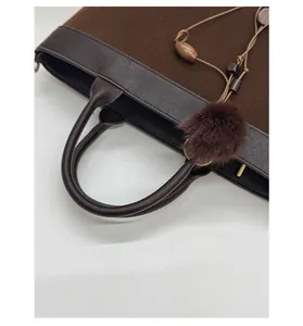 Detail of dark brown tote bag featuring leather trim, suede panels and plush ball charm