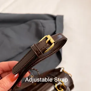 Detalle de la correa ajustable de cuero marrón oscuro con hebilla dorada y costuras finas