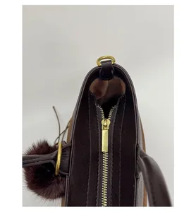 Detail view of smooth golden zipper and fluffy pompom charm on a brown leather handbag