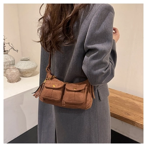 Detail of a brown suede baguette bag featuring front flap pockets and fringe tassels