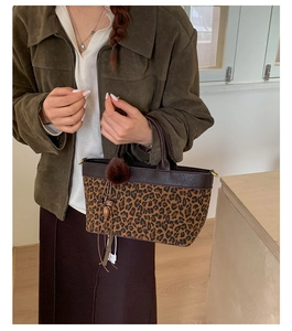 Close-up of leopard print handbag featuring leather trim and a decorative plush pom-pom charm