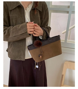 Close-up of caramel suede handbag with plush ball pendant and gold hardware details