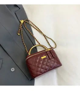 Detail of burgundy quilted bag with golden semicircular handle and chain strap on blazer