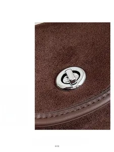 Macro detail of silver oval twist lock and stitching on brown suede saddle bag