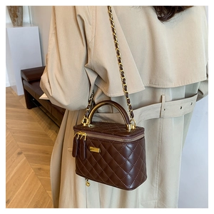 Detail of vintage brown quilted crossbody bag with gold metal handle on a model's trench coat