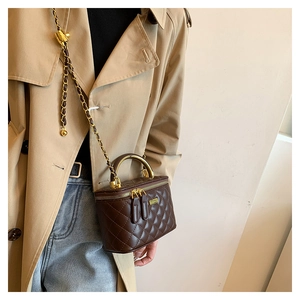 Detail of a brown quilted leather crossbody bag with gold metal handle on a beige trench coat