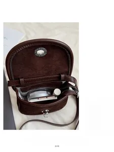 Interior detail of a dark brown suede saddle bag with a zipper pocket and makeup items