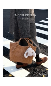 Brown suede tote bag with a cute white bunny pendant carried by a model on a city street