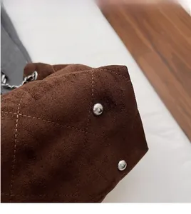 Detailed base of brown suede bucket bag featuring quilted pattern and metal feet