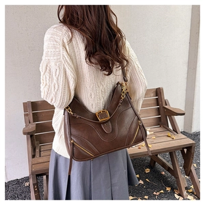 Detail der dunkelbraunen Vintage-Hobo-Tasche mit Goldbeschlägen auf einer Holzbank