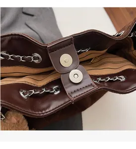 Detail of magnetic buckle, striped lining, and leather chain strap on a brown tote