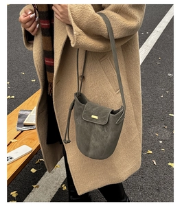 Dettaglio borsa a secchiello in camoscio grigio con fibbia dorata su cappotto beige