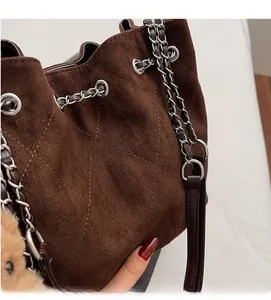 Detail of dark brown quilted suede bucket bag with silver chain strap and plush bear charm