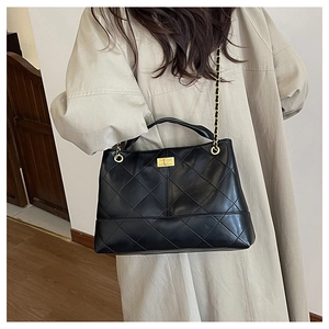 Detail view of black quilted faux leather tote with golden lock and chain strap